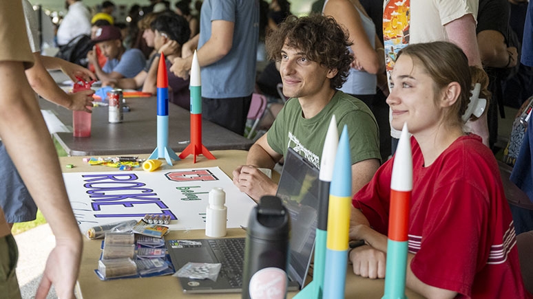 Students at the Club Expo seated at a table with model rockets placed nearby.