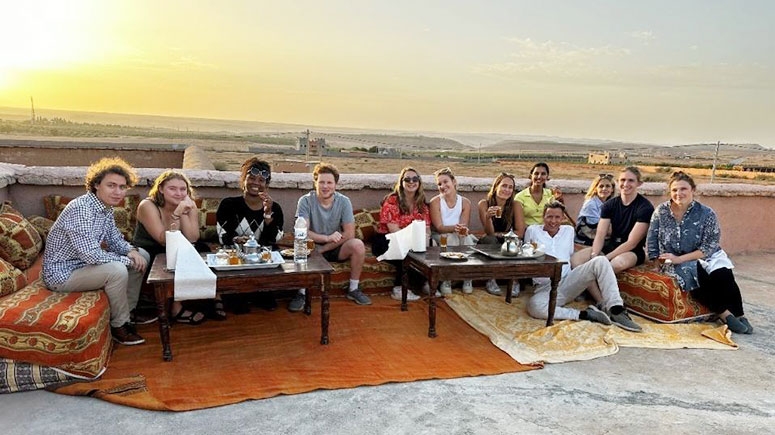 Students on a French term abroad gather around an outdoor table on a sunny day as the sun begins to set in the distance.